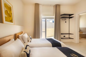 A hotel room with two beds, a large window, a black shelf, and a bathroom visible through the window.