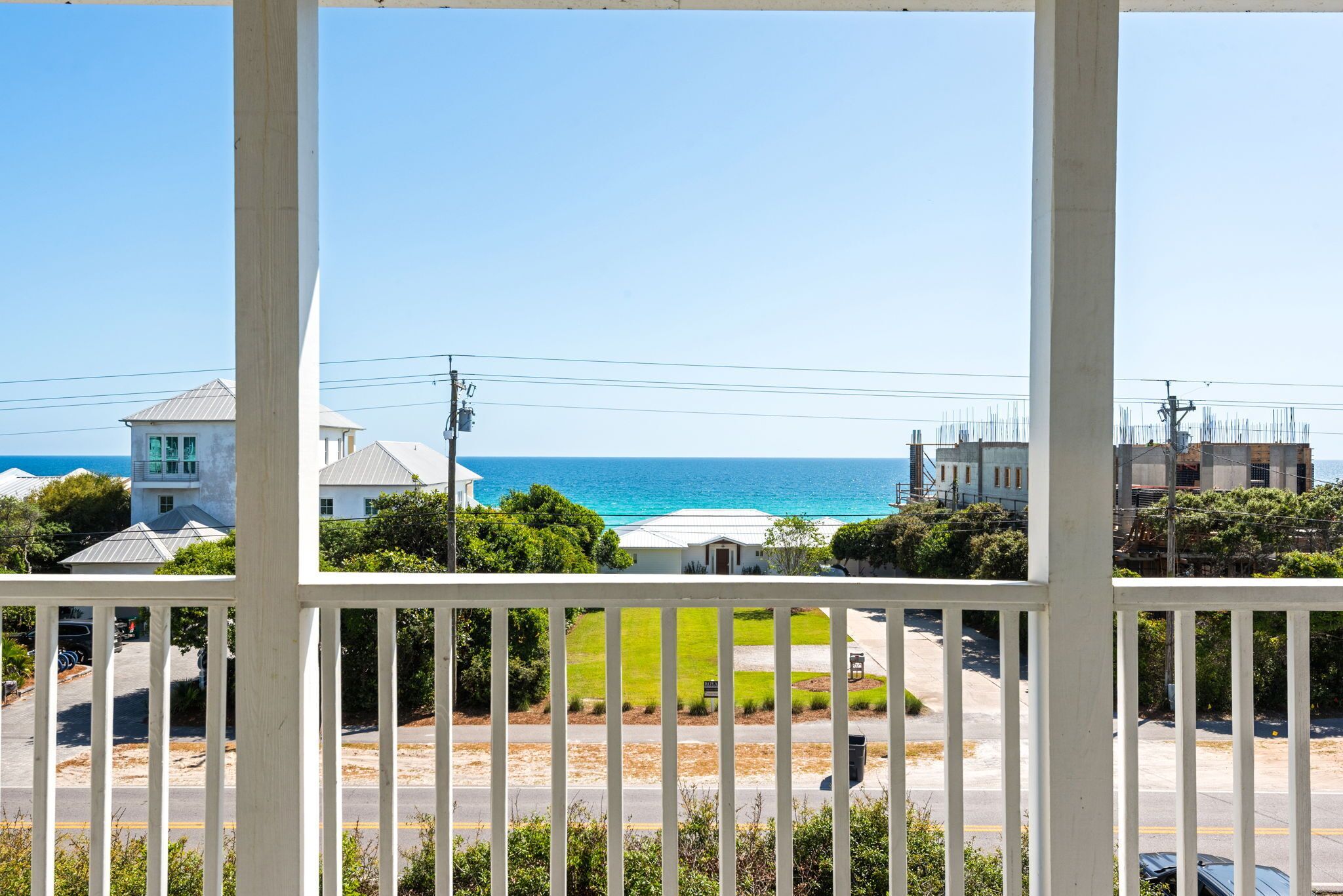 A coastal view from a balcony with a white railing, a road, and buildings in the background.