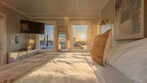Quarto com cama, televisão, vista do porto de iates e porta que dá para uma varanda.