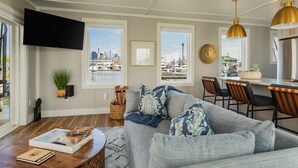 Uma sala de estar com um sofá, uma mesa de centro, uma TV e vista para um porto de iates.