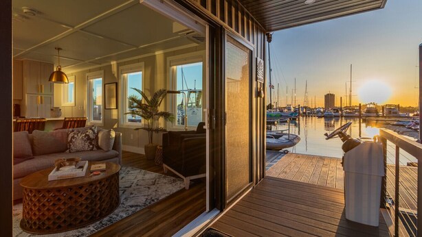 Sala de estar moderna com sofá, mesa de centro e vista para uma marina com barcos.