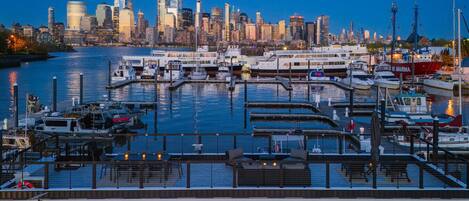 A marina with boats docked, a city skyline in the background, and a modern building with large windows.