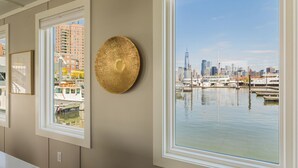 Quarto com uma grande janela com vista para um porto de iates e horizonte urbano, um quadro na parede e um ornamento de parede texturizado.