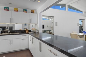 A modern kitchen with white cabinets, a black countertop, and a view to the outside. - Beautiful Canyon View Estates Condo with amazing views (Palm Springs)
