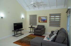 A living room with a ceiling fan, a flat-screen TV, a gray sofa, a gray armchair, and a patterned rug. - 3-bedroom house in Ocho Rios, Richmond Estate with private pool (Plantation Village)
