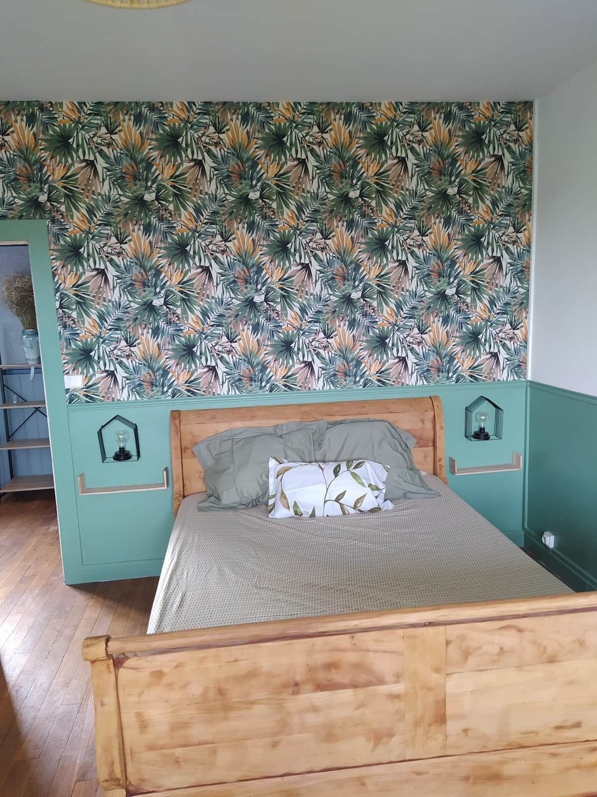 A bedroom with a bed, a wall with a tropical leaf pattern, and a wooden headboard.