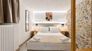 Ein Hotelzimmer mit Bett, Nachttischen, Heizkörper, einer Steinwand und einem gerahmten Bild an der Wand.