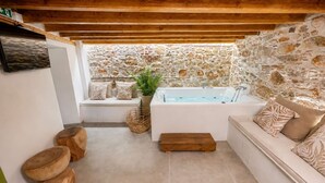 Ein Spa-Raum mit Steinwand, einer Badewanne und einer Sitzecke mit Kissen.