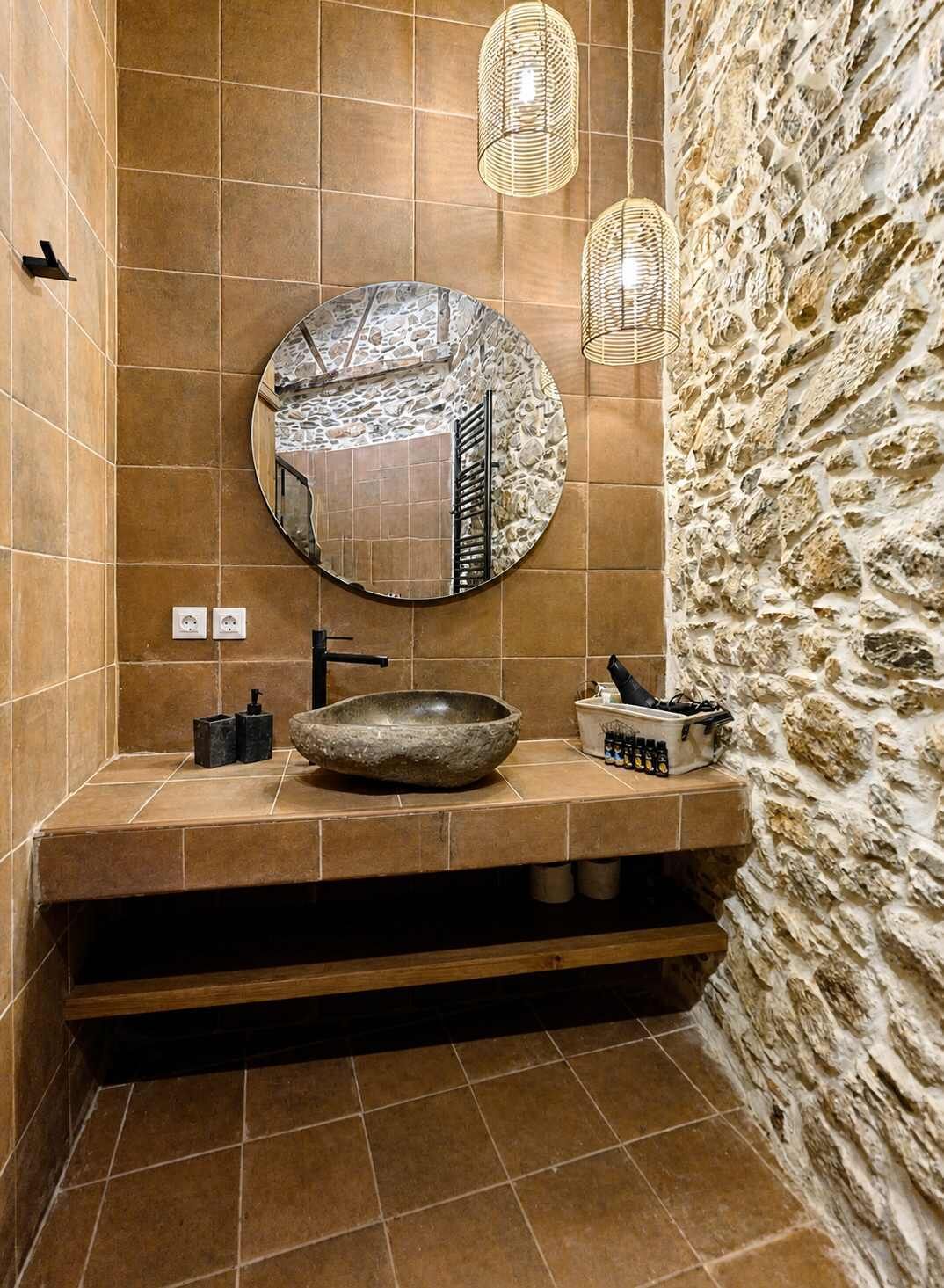 Une salle de bain avec un miroir rond, un lavabo en pierre et deux appliques murales.