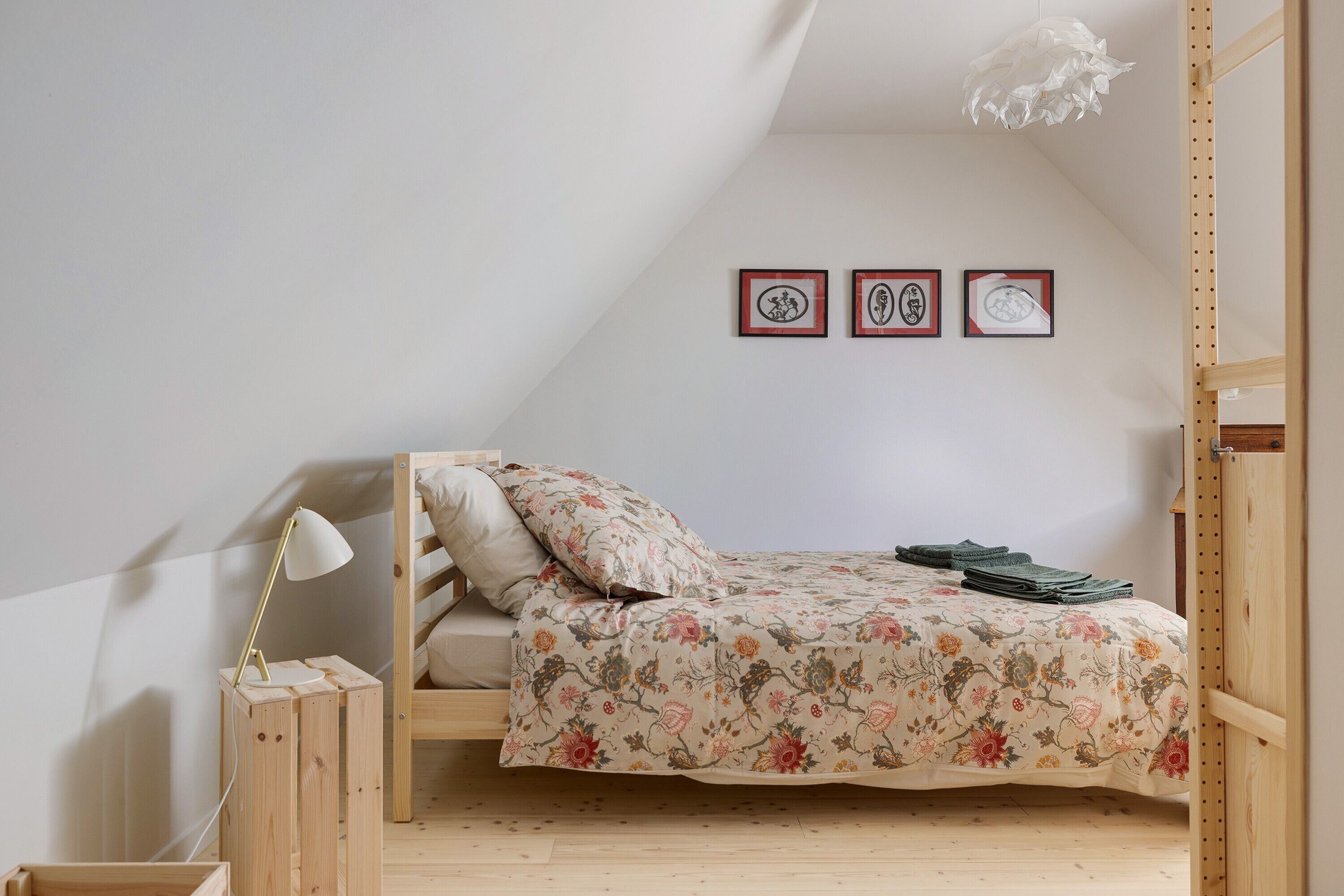 A small, cozy bedroom with a bunk bed, a bedside lamp, and three framed pictures on the wall.