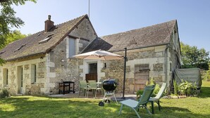Een stenen gebouw met een schuin dak, een barbecue, buitenzitplaatsen en een overdekt terras.
