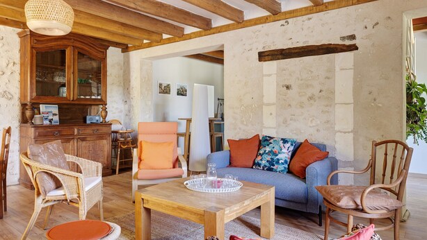 Een rustiek interieur met zichtbare houten balken, een rieten bank, een houten salontafel en een rieten stoel.