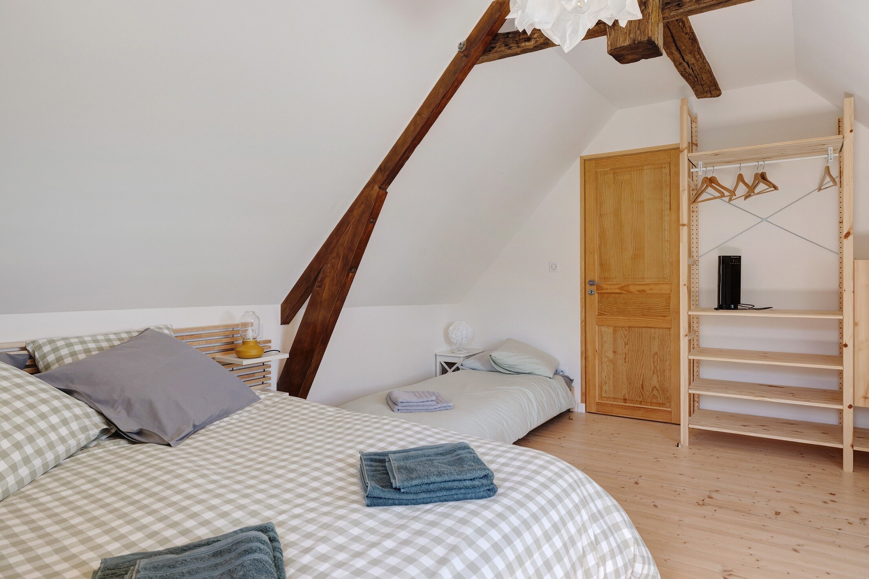 A bedroom with two beds, a wooden wardrobe, and a hanging clothes rack.