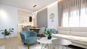 A modern living room with a sofa, armchair, coffee table, and a dining area with chairs and a table.