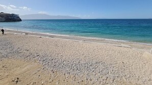 A beach with a rocky shoreline, clear blue water, and distant mountains.