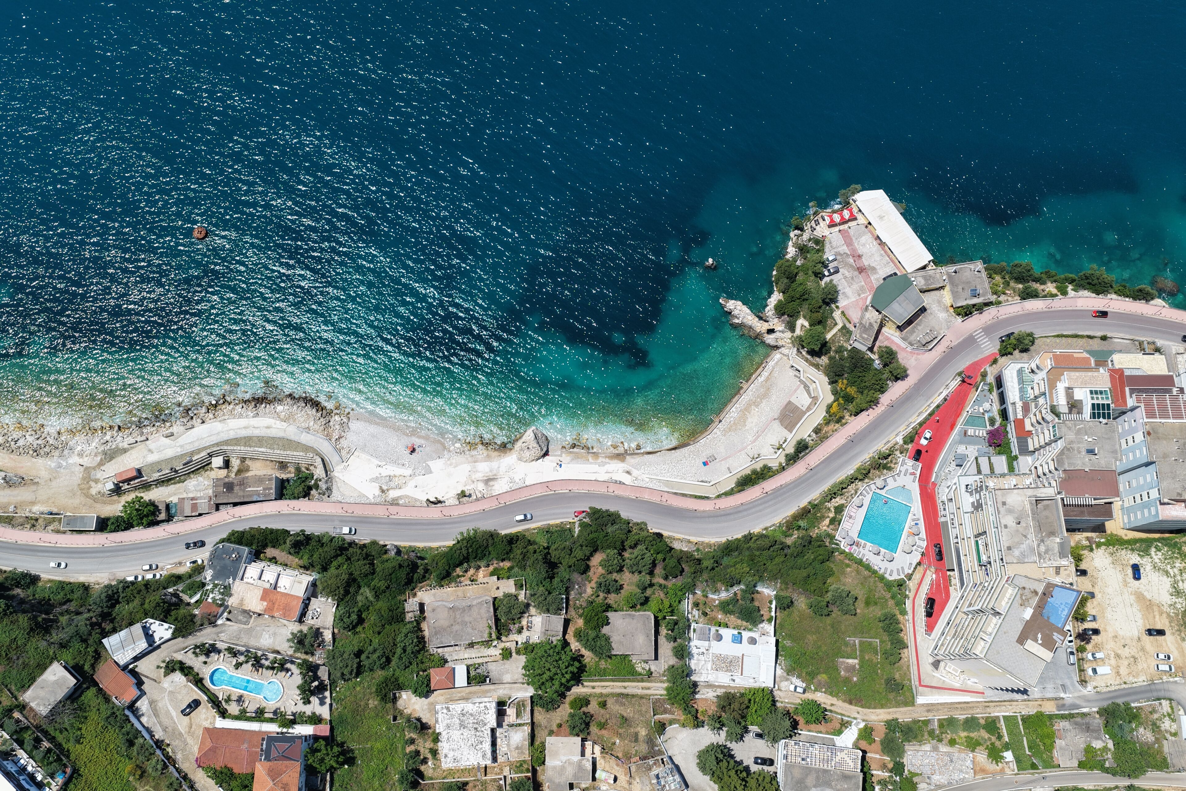 Vista aérea de uma área costeira com uma estrada sinuosa, piscina e edifícios.