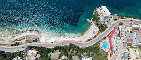 Vista aérea de uma área costeira com uma estrada sinuosa, piscina e edifícios.