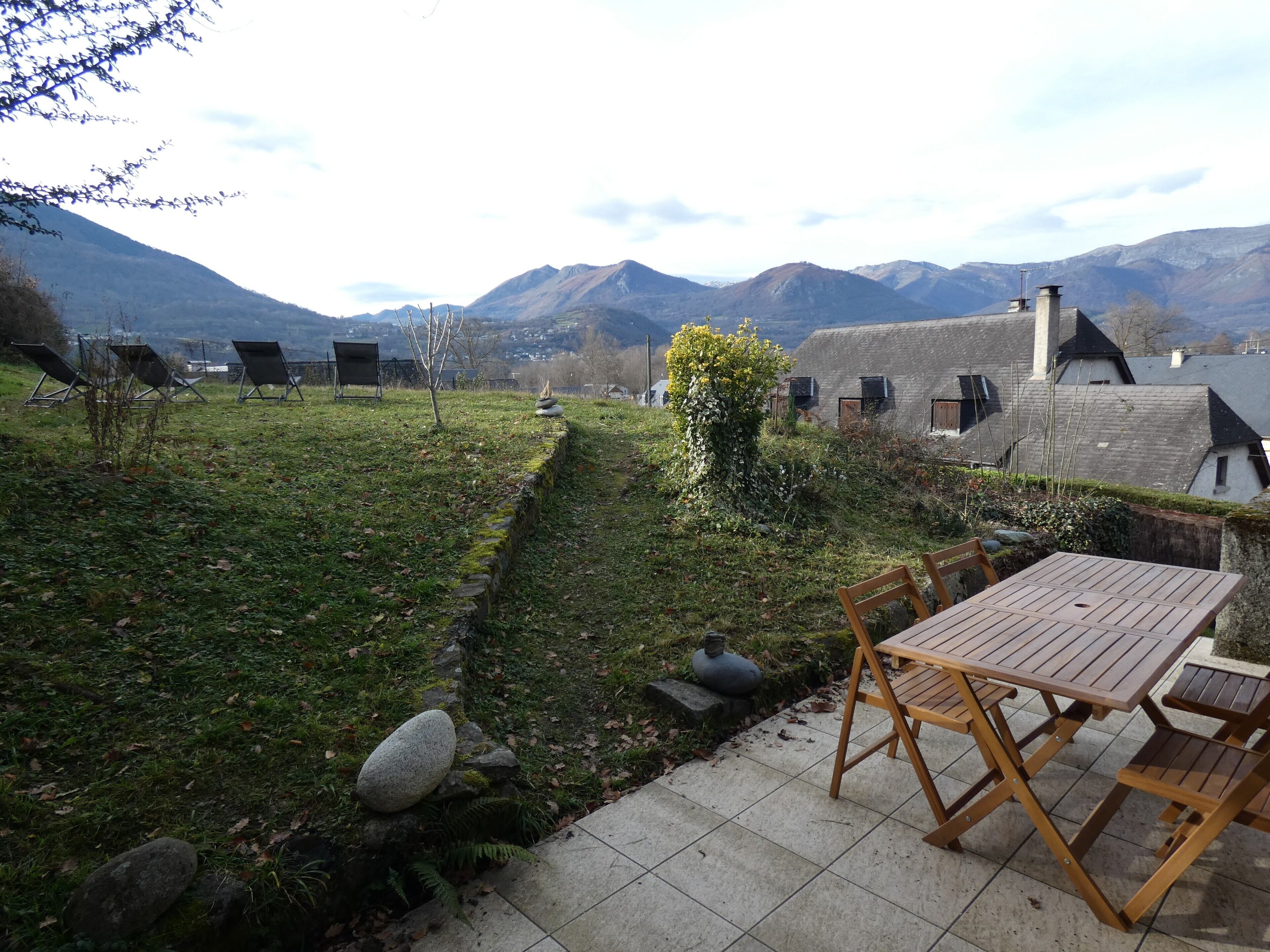 Eine Terrasse mit Tisch und Stühlen, ein Kiesweg und eine Berglandschaft im Hintergrund.