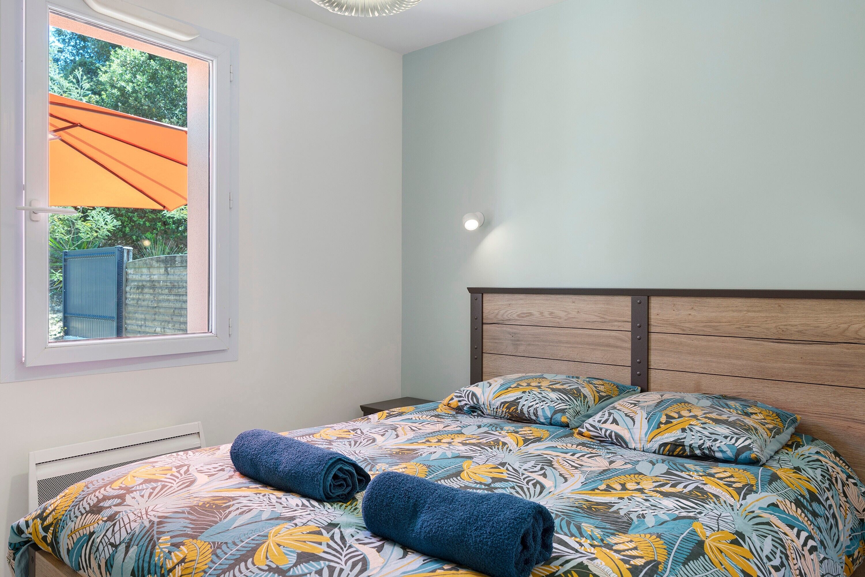 Een slaapkamer met een bed, een raam met een paraplu en uitzicht op groen.