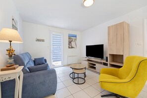 Uma sala de estar com sofá, poltrona amarela, televisão e abajur.