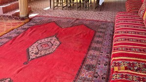 A dining area with a table set for four, surrounded by chairs with striped cushions, a large woven wall hanging, and a patterned carpet. - Tremendous 4-bedroom bed & breakfast in tranquil Imi Ouaddar (Imi Ouaddar)