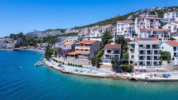 Un pueblo costero con edificios a lo largo del paseo marítimo, un mar azul cristalino y una pequeña zona de playa.