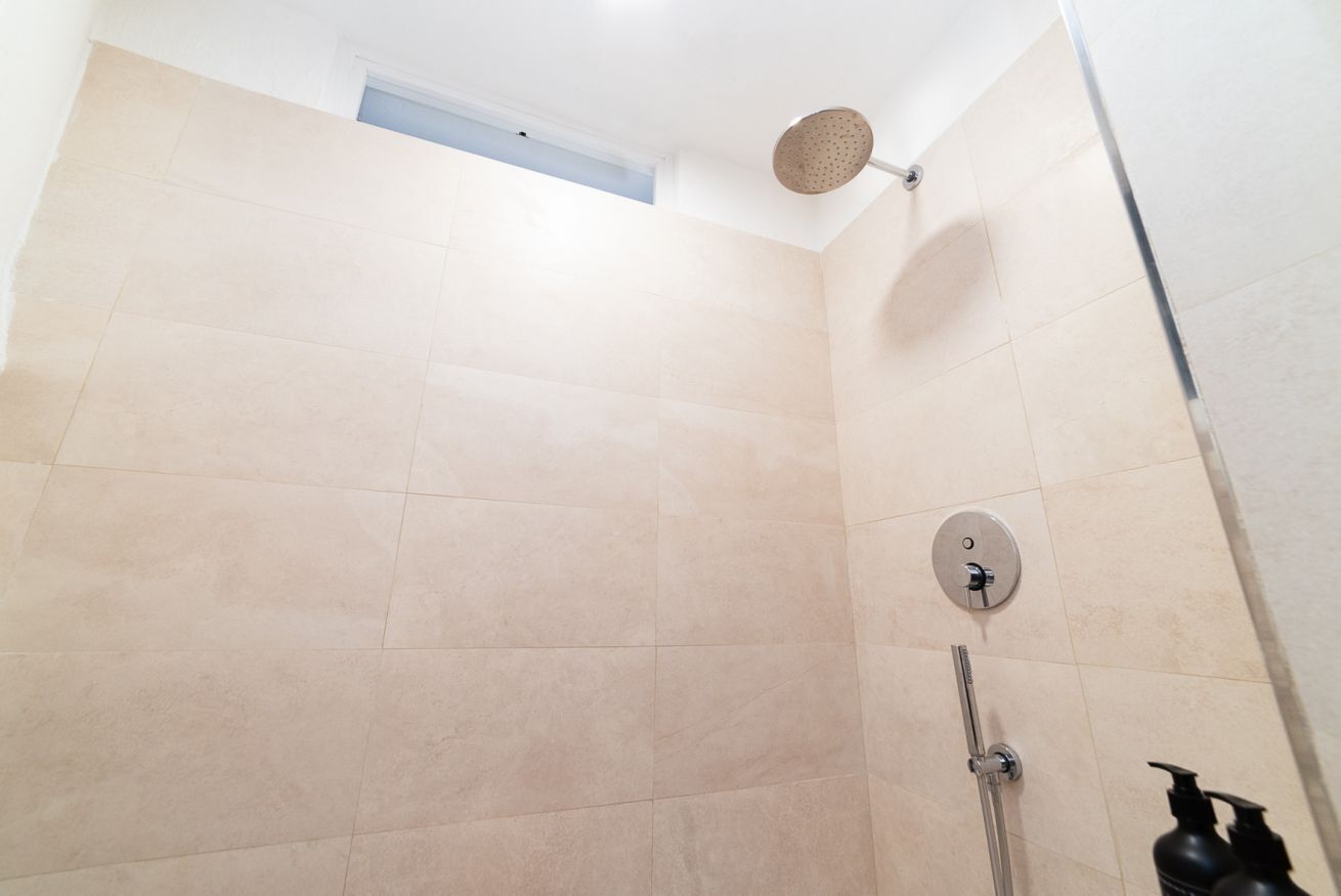 Eine Dusche mit Duschbrause, Wandarmatur und kleinem Fenster darüber.