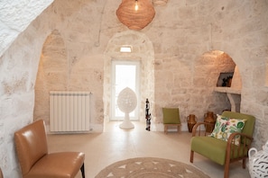 A stone-walled room with a white radiator, a round table, and two chairs. - Villa Euphorbia by Rentbeat (Ostuni)