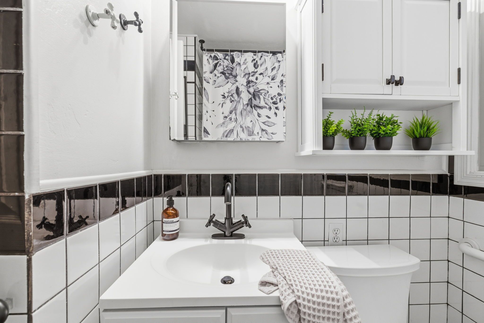 A bathroom with a white sink, a mirror, a shower curtain, and a shelf with potted plants.
