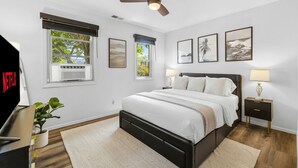 A bedroom with a bed, a ceiling fan, a window with blinds, a wall-mounted air conditioner, and framed pictures on the wall. - Mission Bay Canyon House | Spanish View Retreat (San Diego)