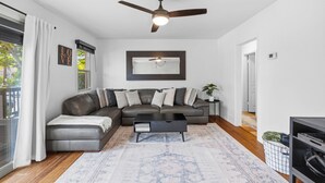 A modern living room with a sectional sofa, a ceiling fan, a coffee table, and a large window with curtains. - Mission Bay Canyon House | Spanish View Retreat (San Diego)