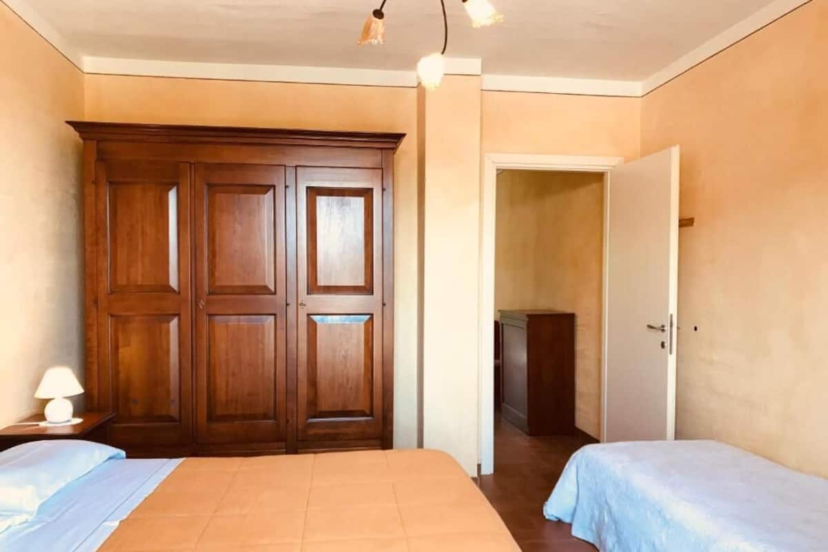 Une chambre dotée d’une grande armoire, de deux lits et d’une porte donnant sur une autre pièce.
