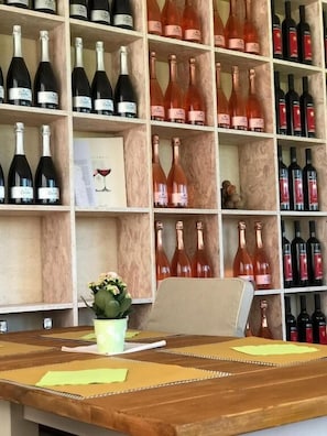 Une cave à vin avec des étagères remplies de bouteilles, une table en bois couverte de papiers et une plante en pot.