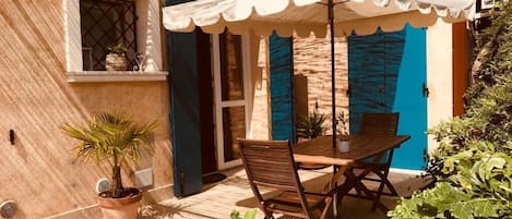 A patio with a table and chairs, a potted plant, and a blue door.