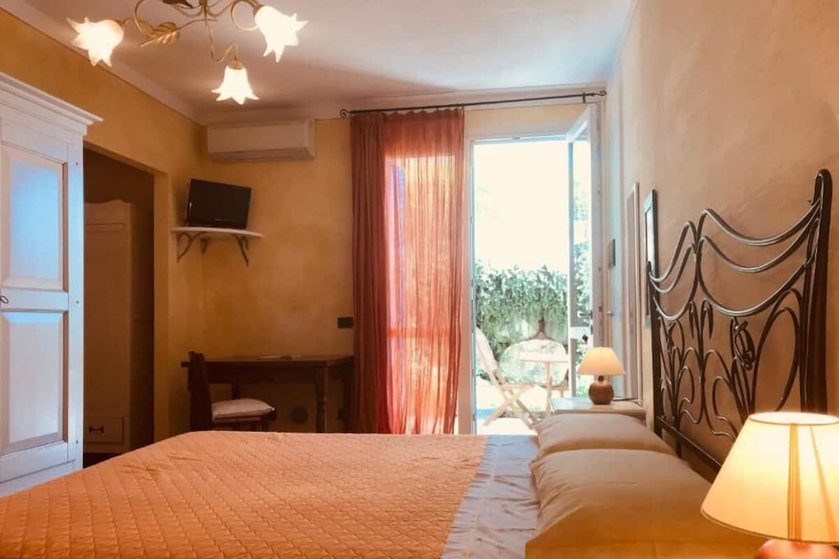Une chambre à coucher comprenant un lit, un bureau, une chaise, un téléviseur et une fenêtre avec des rideaux.