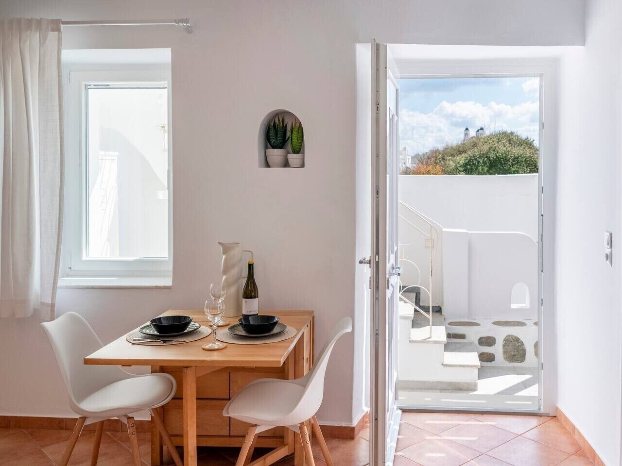 A dining area with a table, chairs, a wine bottle, and a view of a staircase leading to an outdoor area.
