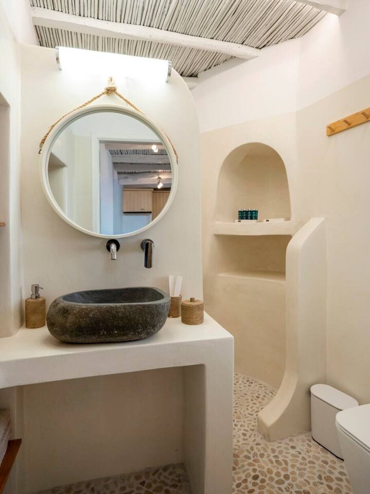 Un bagno con un lavandino in pietra, uno specchio rotondo e una doccia.