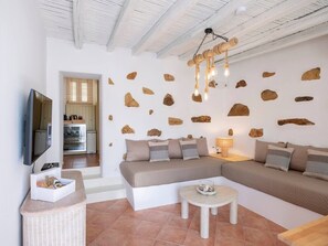 Ein modernes Wohnzimmer mit einem Ecksofa, einem Flachbildfernseher, einem Esstisch und einer Küche im Hintergrund.