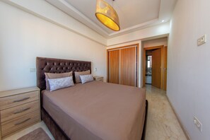 A bedroom with a large bed, a nightstand, a wooden wardrobe, and a ceiling light fixture. - Apartment in the center of Guéliz with swimming pool (Marrakesh)
