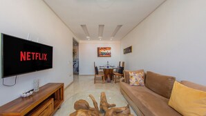 A living room with a flat-screen TV, wooden entertainment unit, brown sofa, and a glass coffee table. - Apartment in the center of Guéliz with swimming pool (Marrakesh)