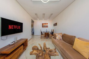 A living room with a flat-screen TV, wooden entertainment unit, brown sofa, and a glass coffee table. - Apartment in the center of Guéliz with swimming pool (Marrakesh)