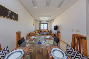 A dining area with a glass-top table, chairs, and a view of a living room in the background. - Apartment in the center of Guéliz with swimming pool (Marrakesh)