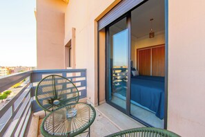 A balcony with two green chairs, a bed with a blue bedspread, and a sliding glass door leading to a room. - Apartment in the center of Guéliz with swimming pool (Marrakesh)