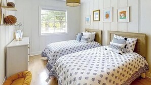 Ein Schlafzimmer mit zwei Betten, einem Fenster und Bildern an der Wand.