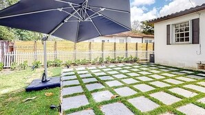 Eine Terrasse mit einem großen Sonnenschirm, einem weißen Zaun und einem Gebäude mit Fenstern.