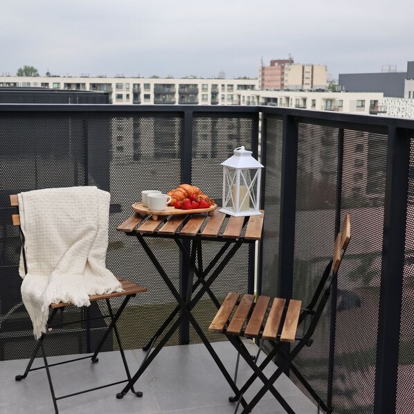 A balcony with a small table, two chairs, a lantern, and a blanket. - Lumina Comfort Apart near ZOO Parking (Łódź)