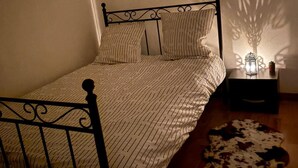 Un letto con struttura in metallo, una coperta a motivi e dei cuscini. C'è un comodino con una lampada e un oggetto decorativo. Un tappeto in pelle di mucca è sul pavimento.