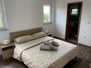 Ein Schlafzimmer mit einem Bett, zwei Nachttischen, einem Fenster und einer Tür zu einem Badezimmer.
