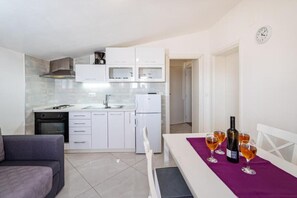 A modern kitchen with white cabinets, a dining area with a table set for two, and a sofa. - Holiday Home Tonka with pool (Donje Raštane)
