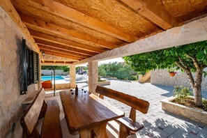 An outdoor patio with stone walls, wooden beams, a bench, and a view of a swimming pool. - Holiday Home Tonka with pool (Donje Raštane)
